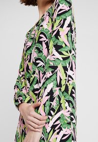 Floral dress featuring a black background with pink and green leaf patterns, long sleeves, and a relaxed fit. Lightweight fabric.