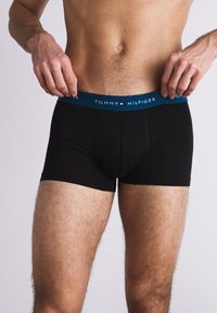 Boxer negros con cinturilla elástica azul que presenta el logo "TOMMY HILFIGER". La tela parece suave y elástica.