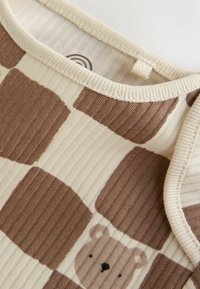 Close-up of ribbed knit beige and brown checkered fabric with a bear face detail near the collar of a garment.