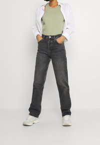 Czarne dżinsy z wysokim stanem o luźnym kroju, zestawione z jasnozielonym prążkowanym topem na ramiączkach i otwartą białą koszulą na guziki.