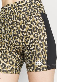 Leopardmønstrede sportsshorts med sorte sidepaneler og et hvidt Adidas-logo på låret, båret af en person.