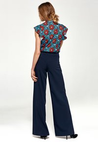 Bluzka w kwiatowy wzór z czerwonymi kwiatami i niebieskimi liśćmi, zestawiona z wysokimi, granatowymi spodniami o szerokich nogawkach, widok z tyłu.