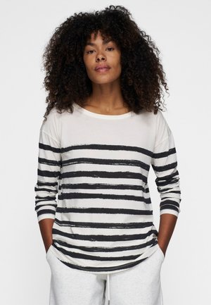 Langarm gestreept shirt in het wit met gedurfde zwarte penseelstreken. Zachte stof, losse pasvorm, ronde halslijn en zichtbare stiksels op de manchetten.