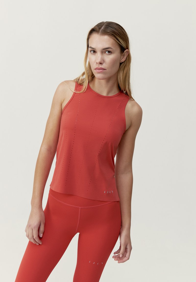 Červený športový top s priliehavým strihom, ktorý má ventilačné otvory a zaoblený lem. Spárovaný s červenými legínami v rovnakom odtieni.