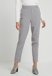 Grijze op maat gemaakte broek met een slanke pasvorm en voorplooien. G gedragen met een geribde witte top en zebra-print hakken. Platte tailleband aan de voorkant.