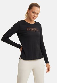 Maglietta nera a maniche lunghe con scollatura rotonda. Presenta testo metallico color rame con la scritta "MENO PERFEZIONE PIÙ AUTENTICITÀ #FREDDY." Tessuto liscio.