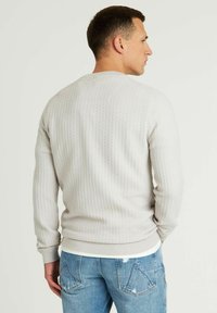 Hellgrauer, strukturierter Sweatshirt mit Rundhalsausschnitt und gerippten Bündchen, kombiniert mit blauen Jeans. Die Rückansicht zeigt ein dezentes Muster und einen gerippten Saum.
