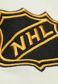 NHL-Logo-Patch in Schwarz mit goldener Stickerei, im Wappen-Design und -Textur auf einem cremefarbenen Hintergrund.