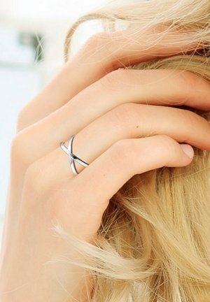 Zilveren crossover ring op een hand met lang haar, met een slank ontwerp en een gladde textuur, die een moderne esthetiek benadrukt.