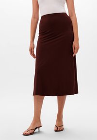Gonna midi bordeaux realizzata in tessuto elastico, con una vita aderente e una silhouette liscia e snella. Abbinata a sandali neri con tacco.