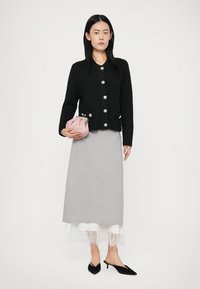 Melnā adīta kardigāna ar sudraba pogām, apvienota ar pelēku midi svārku ar mežģīņu maliņu. Tur rokās mazu rozā sajūgu. Uz kājām melnas mūlas.