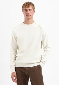 Licht crème geribd trui met een ronde halslijn en raglanmouwen, gecombineerd met een paar bruine corduroy broek. Eenvoudig en met een gestructureerd ontwerp.
