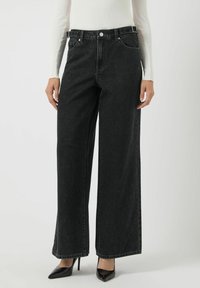 Jeans de mezclilla negros de pierna ancha con cintura alta, diseño de cinco bolsillos y cierre de botón metálico. Tela texturizada y acabado de dobladillo limpio.