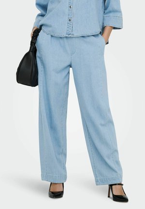 Pantalon large en denim bleu clair assorti à une chemise en denim, chaussures à talons hautes noires et sac à main noir avec poignée froncée.