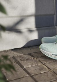 Pair of light blue running shoes resting on textured stone pavement with shadowed wall background.