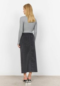 Maglietta grigia a maniche lunghe con righe abbinate a una gonna maxi grigia scura con tasche, taglio dritto e orlo sfilacciato. Mules argentati con tacco completano il look.