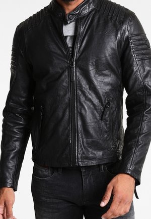 Homme portant une veste en cuir noir de motard avec des détails matelassés aux épaules et aux bras, fermeture éclair frontale et poches zippées, associée à un jean foncé.