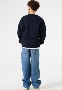 Sudadera azul marino con cuello redondo, corte relajado y puños de canalé, combinada con jeans de corte holgado en azul claro y zapatillas blancas.