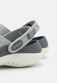 Szare Crocsy z teksturowaną górą, kontrastującym ciemnoszarym paskiem i białą lekką podeszwą, z logo "crocs" i "LITE" na boku.