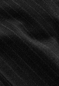 Tissu noir avec fines rayures blanches et plis subtils créant une surface texturée légèrement ondulée.