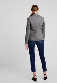 Grau gestreifter Blazer mit tailliertem Design, kombiniert mit dunkelblauen Jeans. Der Blazer verfügt über eine maßgeschneiderte Silhouette und strukturierte Schultern.