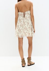 Vestido de tirantes finos con estampado floral en beige claro, con un escote con volantes y un diseño de espalda con abertura. Combinado con botas de tobillo marrones.