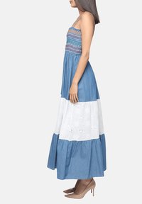 Vestido maxi con un corpillo azul fruncido, una capa blanca bordada y un dobladillo con volantes azul, con finas tirantes y un diseño fluido.