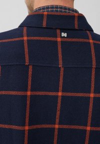 Navy shirt met een oranje ruitpatroon, met een button-down kraag en een zilveren logo-label op de achterkant van de halslijn. Getextureerde stof.