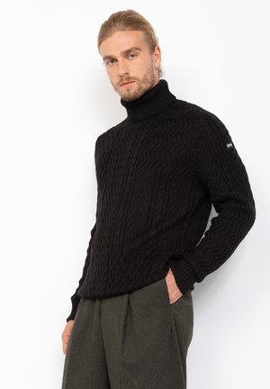 Suéter negro de cuello alto de punto con un diseño de trenzado texturizado, con un cuello ajustado y puños acanalados, combinado con pantalones oscuros de tiro alto.