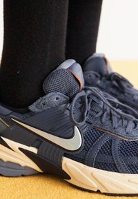 Marineblaue Nike-Sneaker mit strukturiertem Mesh und synthetischen Überzügen. Mit einem silbernen Swoosh-Logo und einer cremefarbenen Sohle. Darunter schwarze Socken.