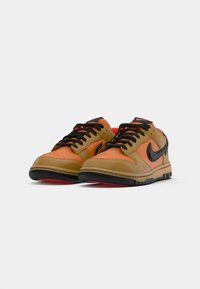 Nike sneakers featuring a mix of orange and tan leather with black accents, textured toe box, and a black rubber sole with red details.