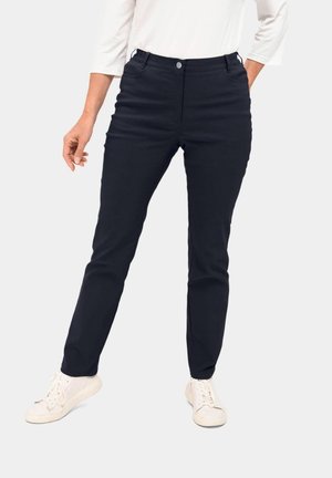 Pantalons bleu marine à coupe slim, avec fermeture à bouton, poches avant et un tissu lisse et texturé. Associés à des baskets blanches.