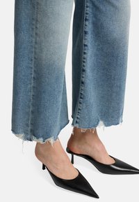 Jeans ampi in denim azzurro con orli sfilacciati, abbinati a mule nere con punta a stiletto.