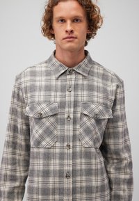 Grau-weiße kariert Flanellhemd mit einem Kragen, zwei Brusttaschen und Knopfverschlüssen, aus einem strukturierten Stoff und mit langen Ärmeln.