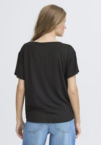 Tricou negru cu mânecă scurtă, cu o croială lejeră, decolteu rotund și material din bumbac moale, asortat cu blugi din denim de culoare albastru deschis.