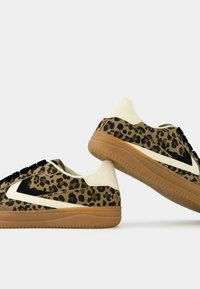 Leopard-print sneakers featuring a mix of brown and cream materials, black detailing, and a tan rubber sole. Laced front with padded collar.