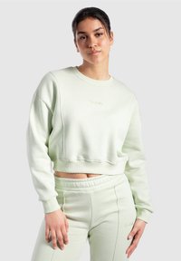 Sudadera cortada de color verde menta con puños y cinturilla de canalé, que presenta un sutil logo bordado en el pecho, combinada con joggers a juego.