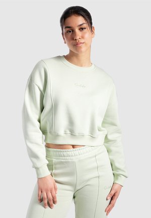 Mintgrøn cropped sweatshirt med ribbede manchetter og talje, med et diskret broderet logo på brystet, parret med matchende joggers.