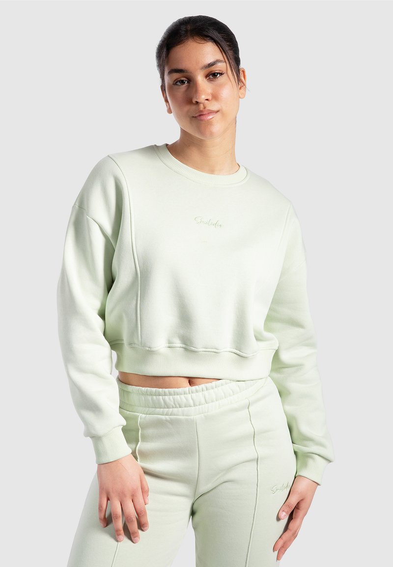Mintgrön cropped sweatshirt med ribbad mudd och midja, med en subtil broderad logotyp på bröstet, ihopparad med matchande joggers.