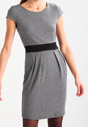 Woman wearing a black and white small checkered fitted dress with cap sleeves and a wide black waistband.