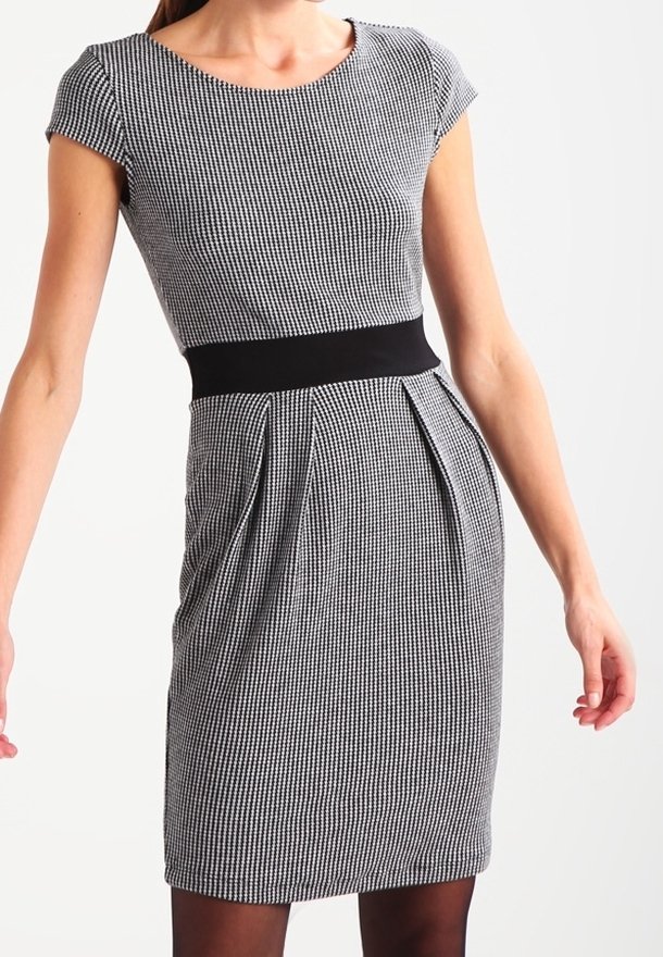 Femme portant une robe ajustée à petits carreaux noir et blanc avec des manches courtes et une large ceinture noire.