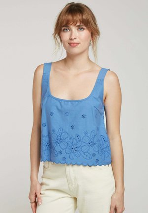 Débardeur en coton bleu avec décolleté carré, ourlet à volants et détail de broderie florale en bas. Les bretelles sont larges et plates.