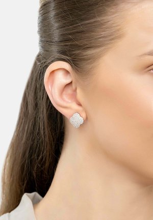 Silver stud earrings feature a textured, floral design with a polished finish, worn on the right ear against smooth, straight hair.