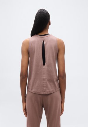 Persona de espaldas vistiendo un top sin mangas color malva con un corte vertical en forma de ojo de cerradura en la parte trasera y pantalones sueltos a juego, sobre un fondo liso.