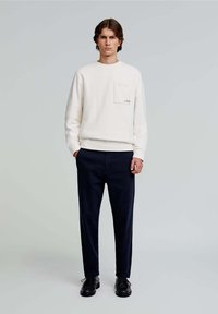 Krémová bavlněná mikina s přední kapsou, v kombinaci s tmavě námořnickými kalhotami. Outfit doplňují černé šněrovací boty.