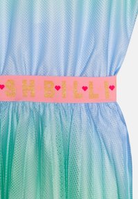 Světle modré a zelené síťované šaty s růžovým pruhem, na kterém je nápis "SHBILLI" zlatým třpytem. Tkanina má měkkou, vzdušnou strukturu s vrstveným vzhledem.