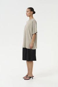 Oversized beige t-shirt with a round neckline, paired with black knee-length shorts. Black flip-flops complete the outfit.
