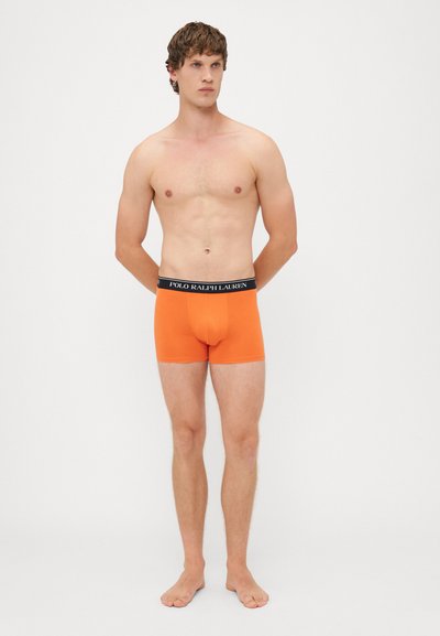Oranžové boxerky s černým páskem, na kterém je nápis "POLO RALPH LAUREN". Materiál je hladký a elastický, navržený pro pohodlí.