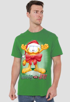 Grünes Baumwoll-T-Shirt mit einer cartoonhaften Katze in einem Weihnachtsmann-Hut, umgeben von einer großen roten Schleife, mit dem Text "Entfalte die Freude!" in festlichen Farben.