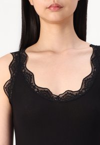 Top sin mangas negro de canalé con un escote redondeado adornado con encaje. El encaje presenta patrones florales y bordes festoneados, añadiendo un detalle delicado.
